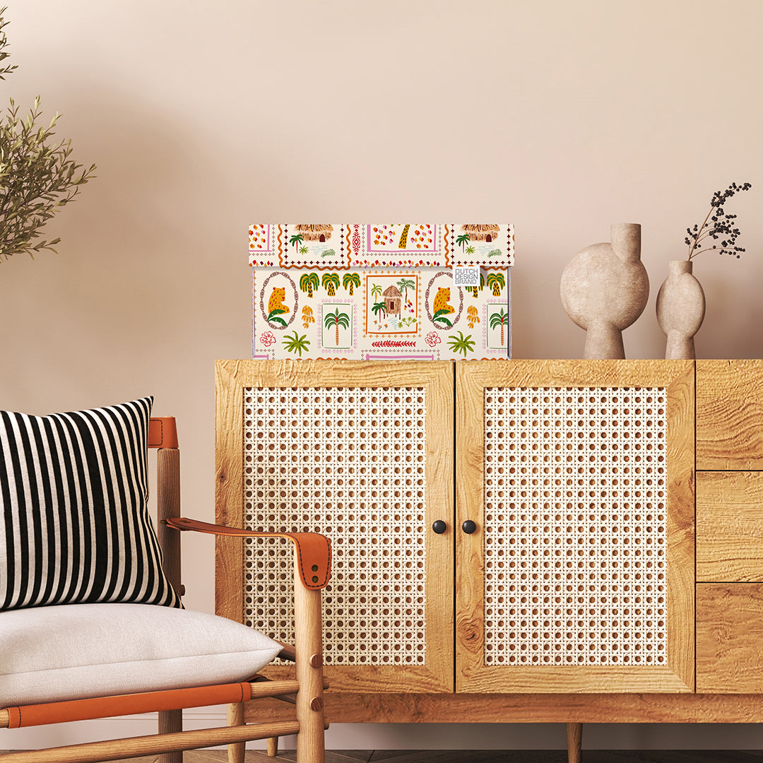 Opbergdoos met tropische print met palmbomen, rieten huisjes en kleurrijke details in een woonkamer.
