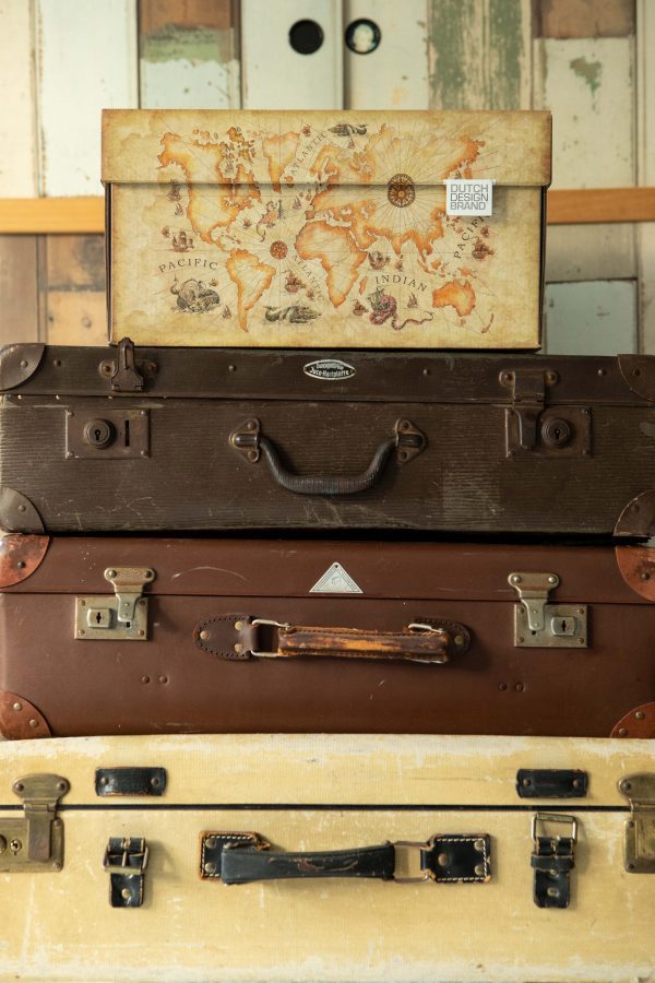 Storage box with an image of an old world map. The box has the color of old faded paper. The box is placed on a stack of suitcases.