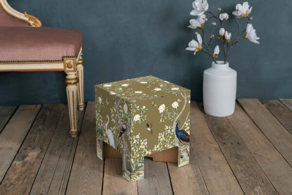 A Dutch Design Brand Chair adorned with the Golden Paradise design, showcasing a variety of birds such as a peacock and a white heron amidst lush flora and fauna on a gold background. The box is detailed with illustrations of blooming white flowers, lemon fruits, and dragonflies.