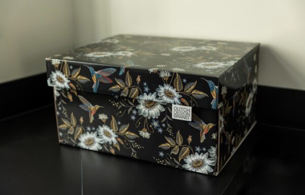A storage box adorned with the "Hummingbirds in the Night" design, featuring a black background with intricate illustrations of colorful hummingbirds in mid-flight, surrounded by large white flowers with golden centers, and an array of green foliage and smaller flowers.