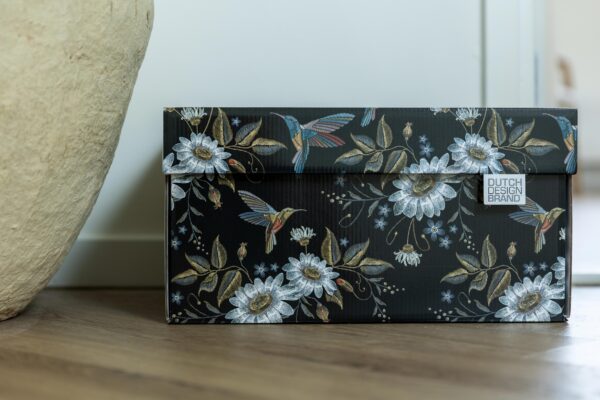A storage box adorned with the "Hummingbirds in the Night" design, featuring a black background with intricate illustrations of colorful hummingbirds in mid-flight, surrounded by large white flowers with golden centers, and an array of green foliage and smaller flowers.